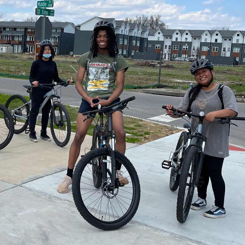 Teenagers on bikes pose on a wide sidewalk