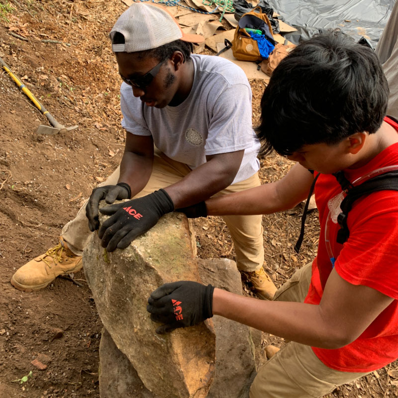 Two young men work together to move a large rock