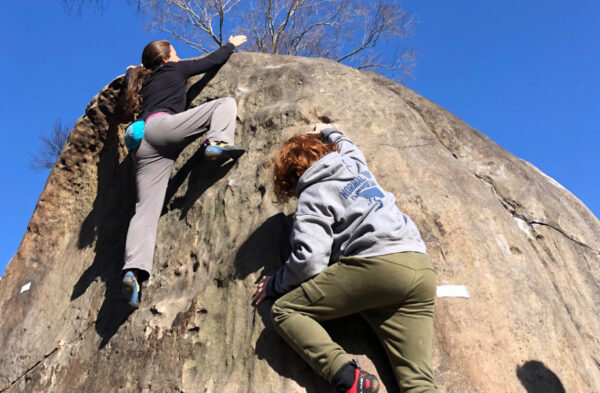 Two young people climb a boulder.