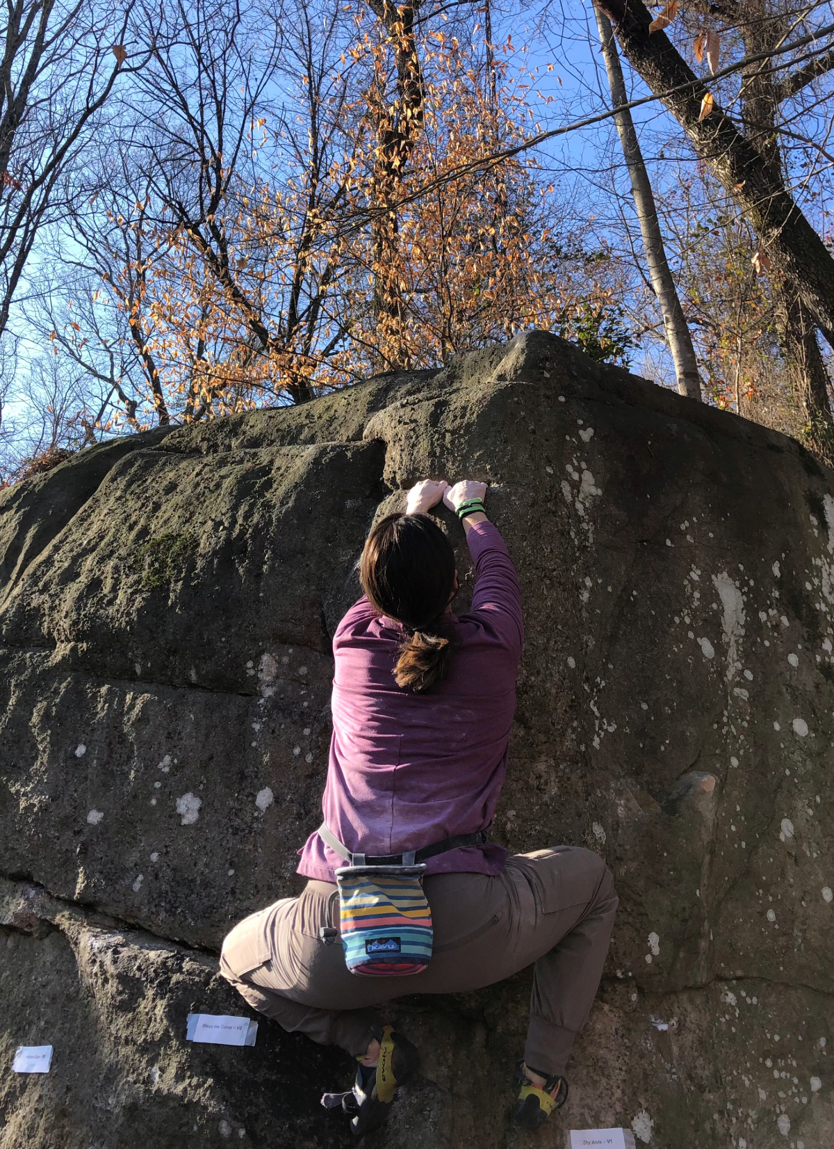 A woman climbs a boulder.