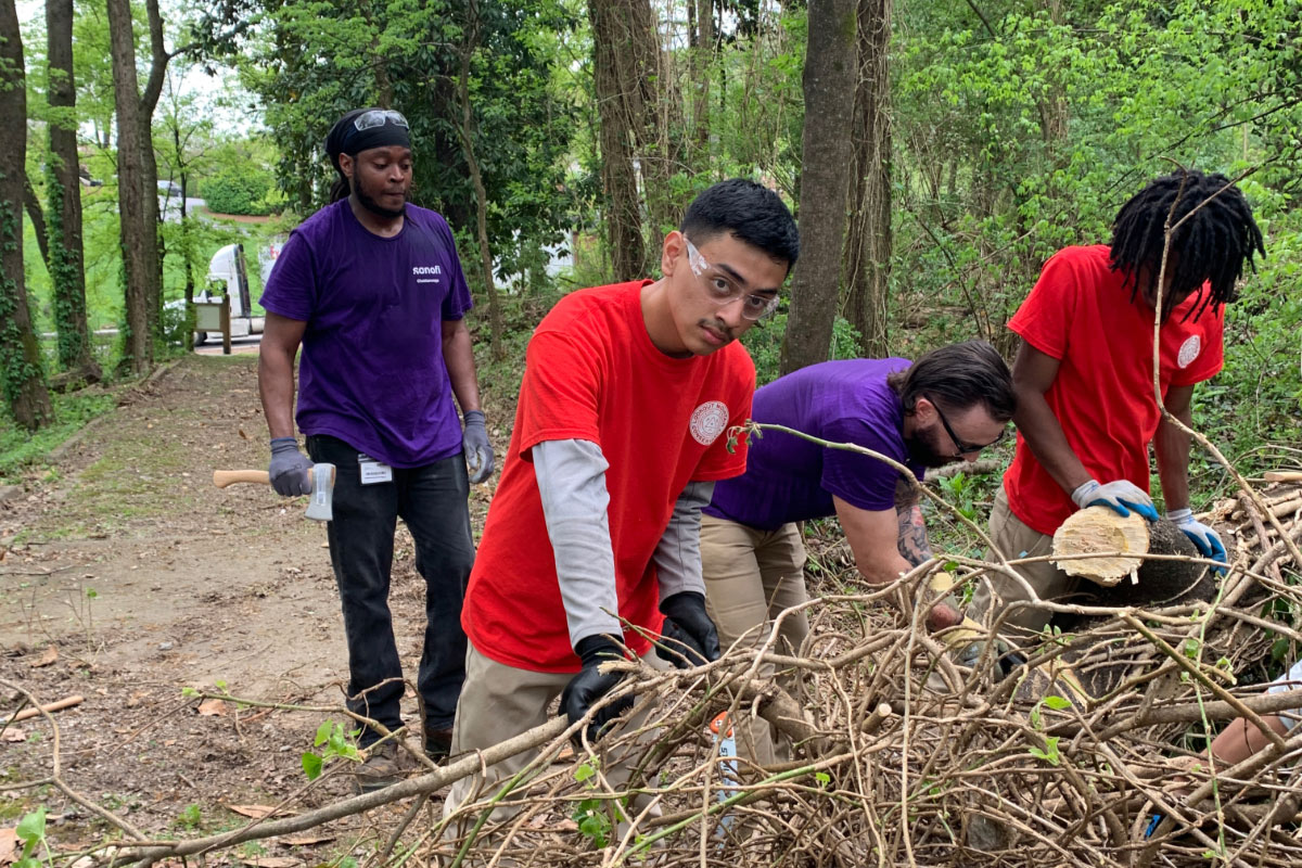 A young Latino male looks at the camera while moving brush with three other men.