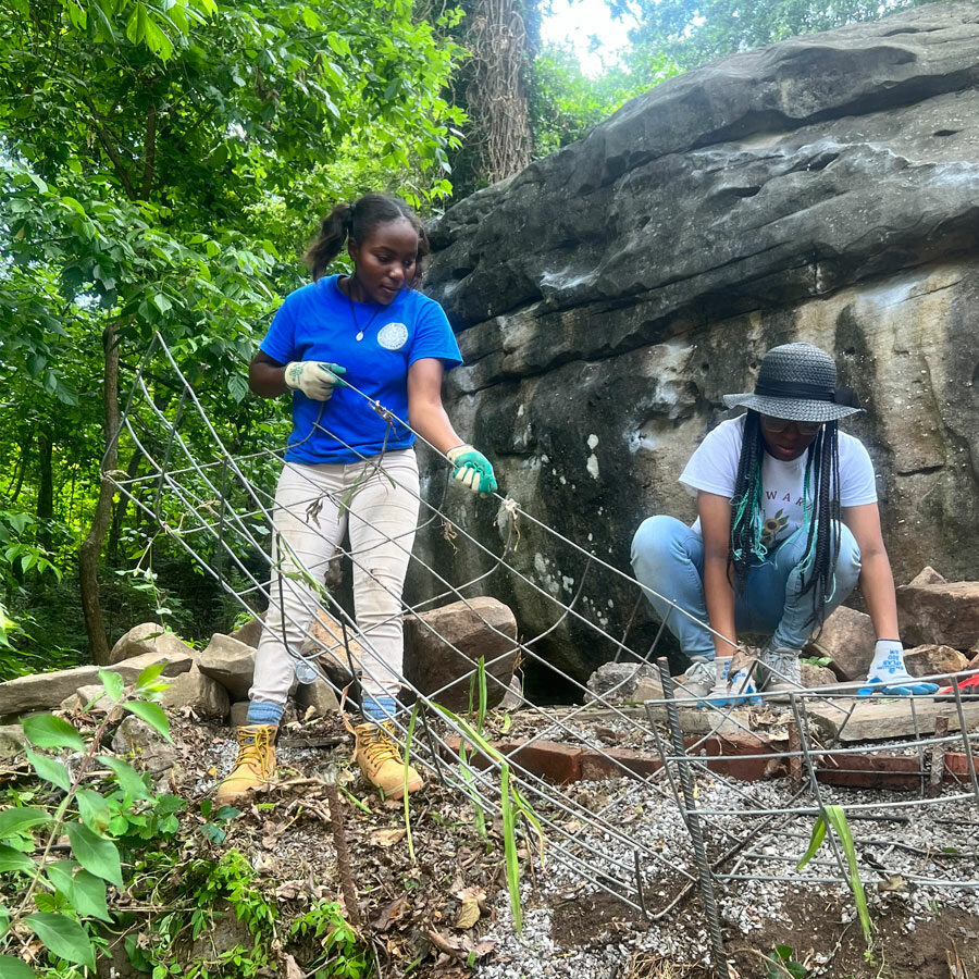 Two black female teenagers build a rock wall at the base of a boulder