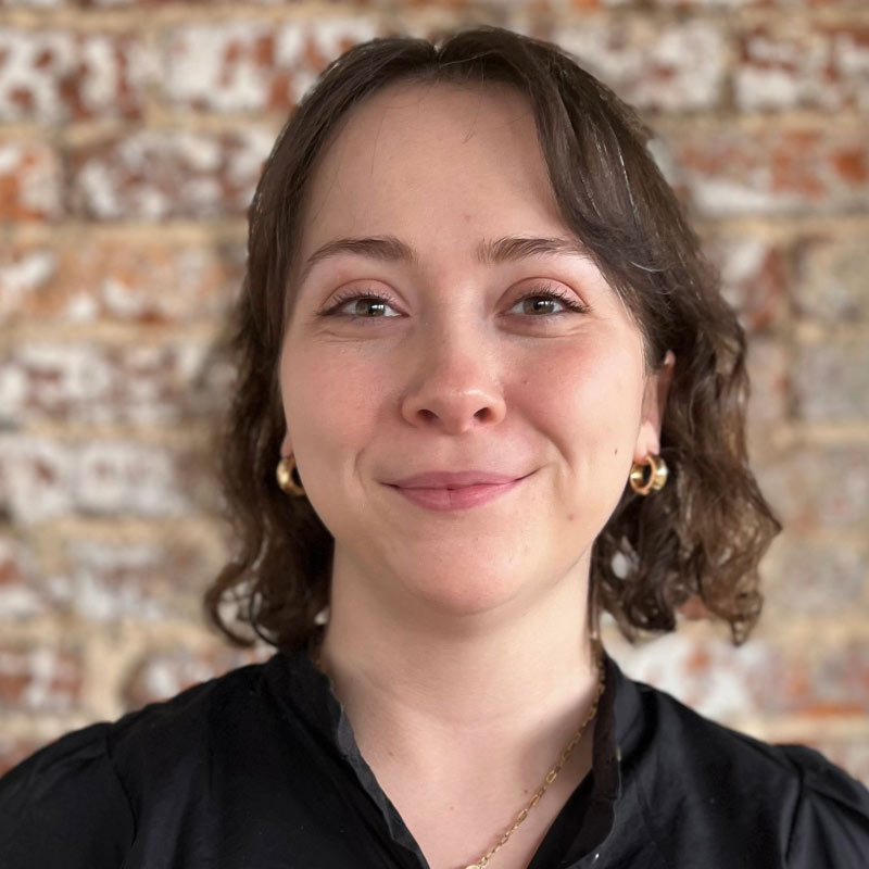 Headshot of a young white female with dark brown wavy hair and wearing a black blouse