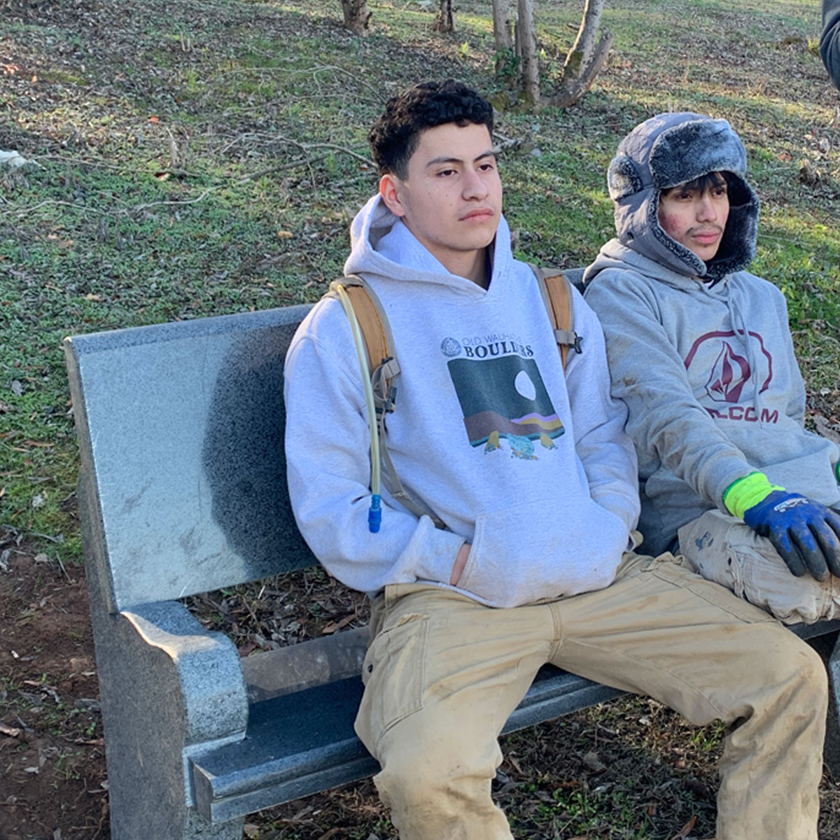 Two young Hispanic males sit contemplatively on a granite park bench