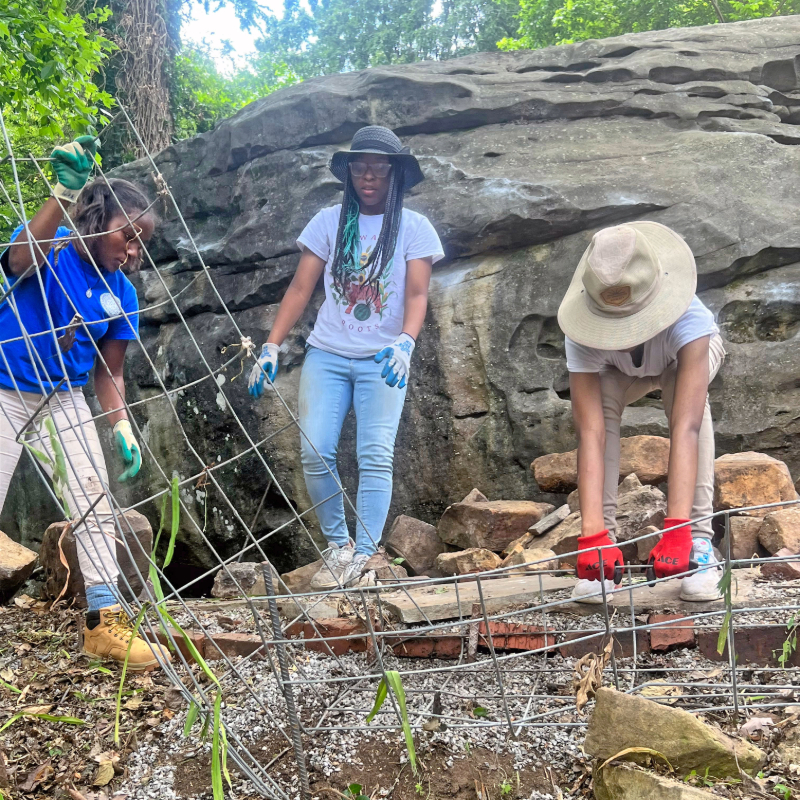 Three young women moving metal frames with a boulder in the background.