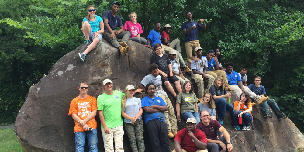 group of youth works sitting o a boulder and smiling