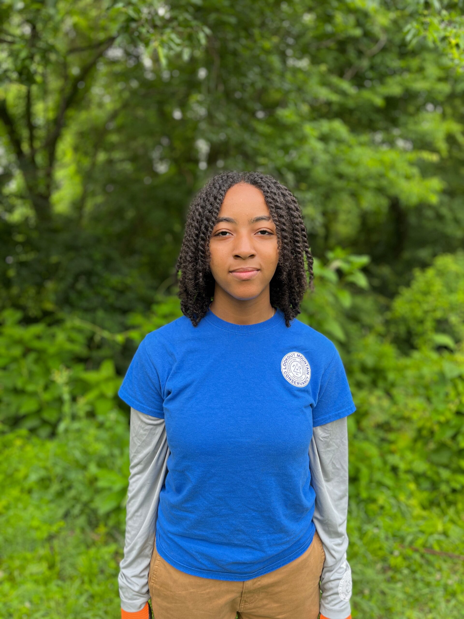 Young black female smiling in a blue shirt in front of a forest backdrop.
