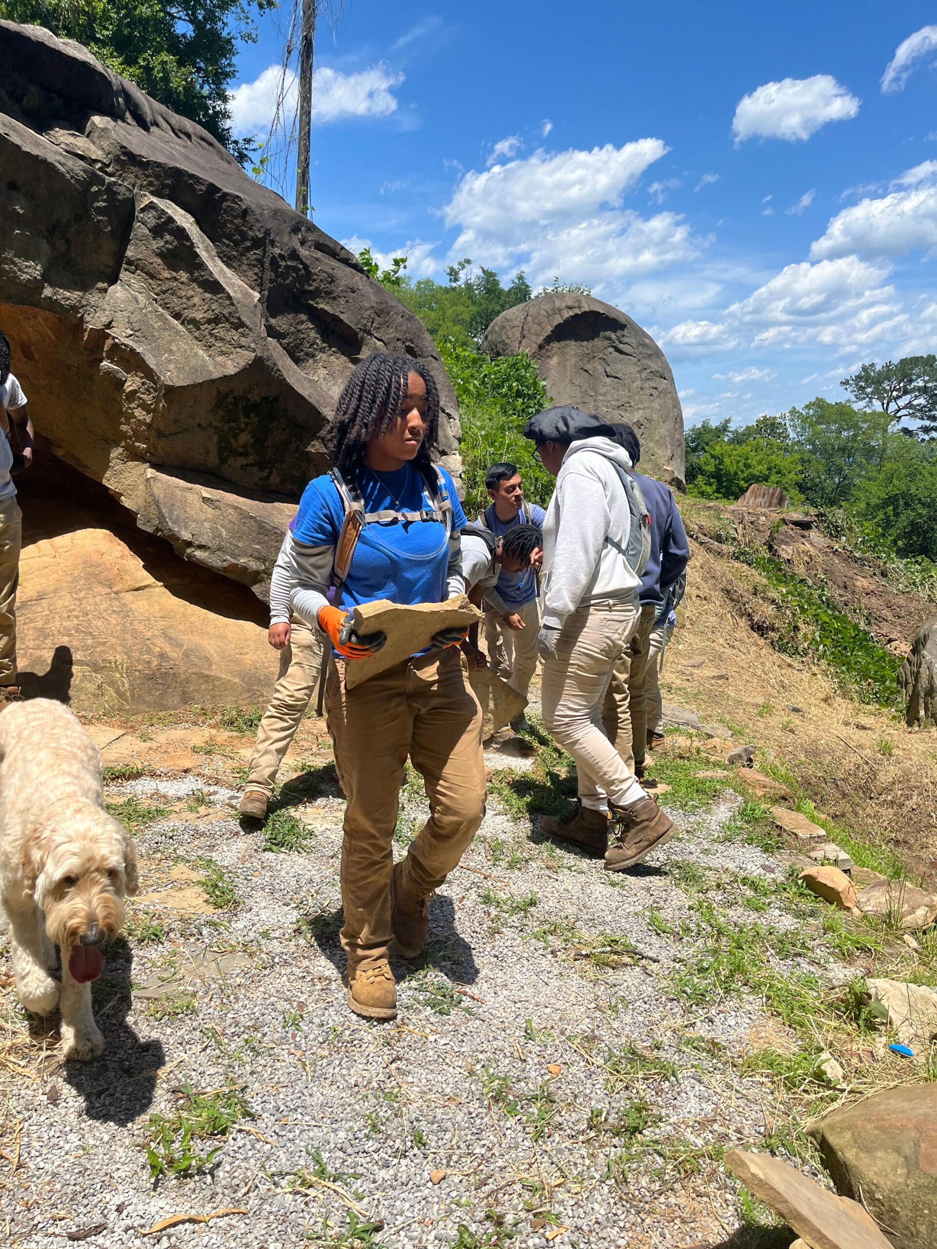 young black female in a blue shirt carrying a stone at a worksite.